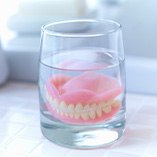 Full set of dentures in a glass of clear fluid on a tiled countertop